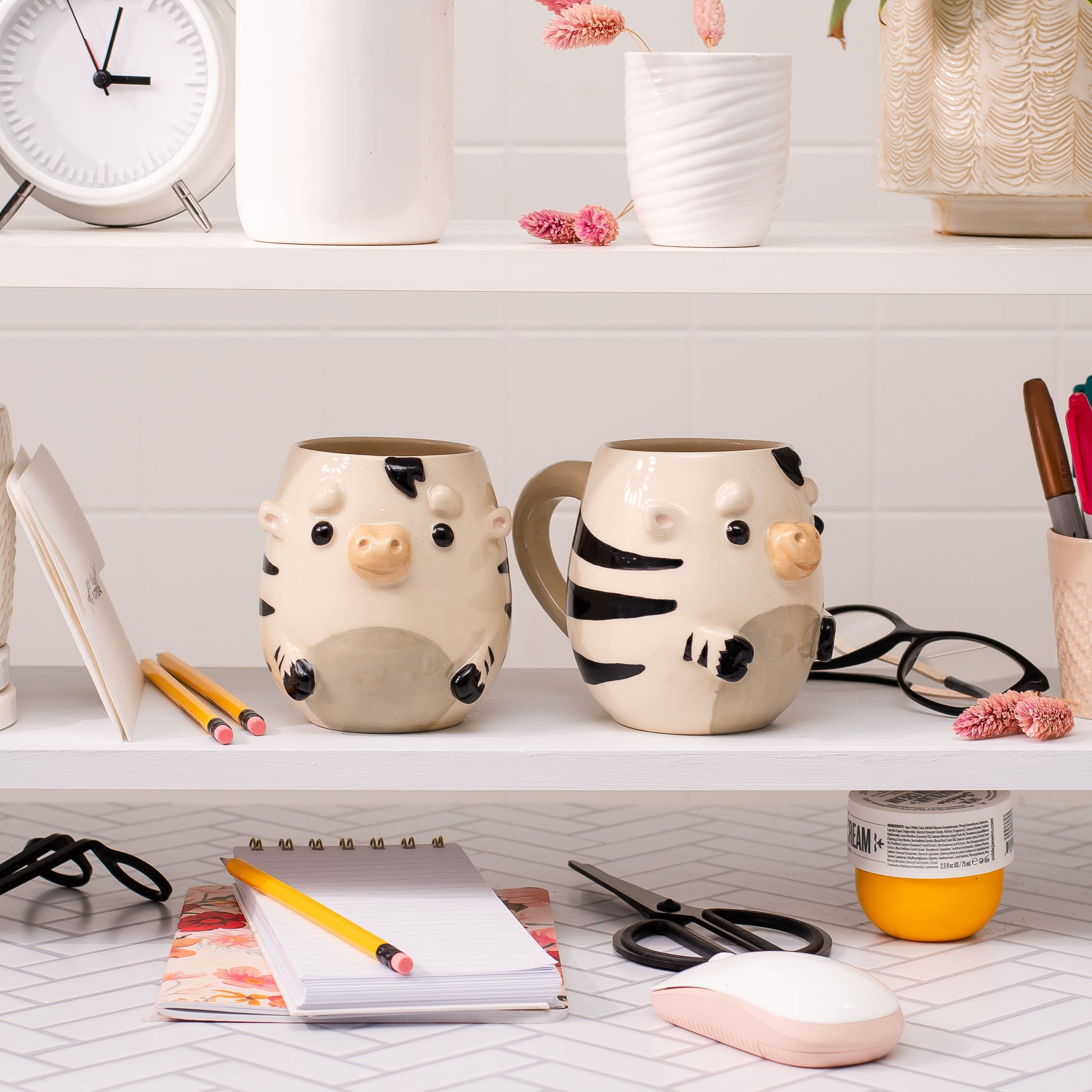 Shelf with decorative mugs, stationery items, and a clock.
