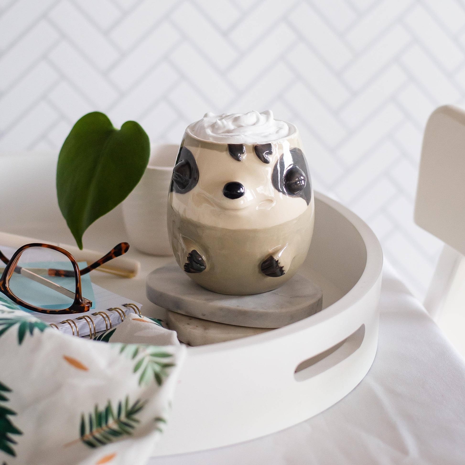 Ceramic sloth-shaped container on a small round table with a white textured wall in the background.