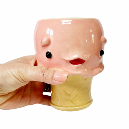 A hand holding a pink ceramic novelty mug shaped like an ice cream cone, against a plain white background.